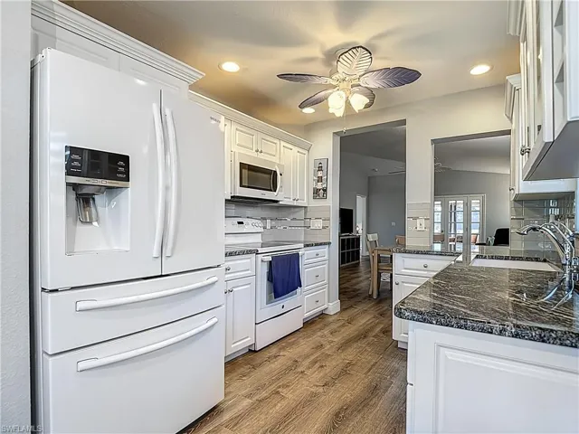 Kitchen featuring white appliances, a ceiling fan, white cabinetry, dark stone countertops, and recessed lighting