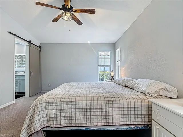 Bedroom with carpet, a barn door, a textured wall, connected bathroom, and ceiling fan