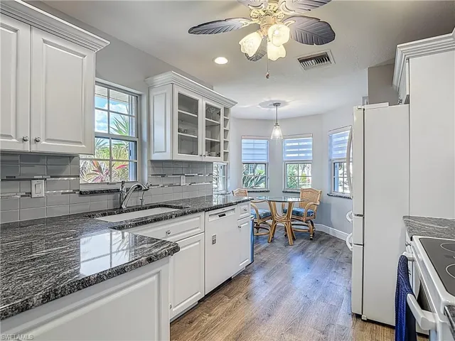 Kitchen with dark stone countertops, glass fronted cabinets, white cabinetry, and hanging light fixtures