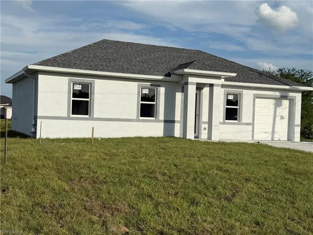 Ranch-style home featuring an attached garage, stucco siding, a front lawn, and roof with shingles