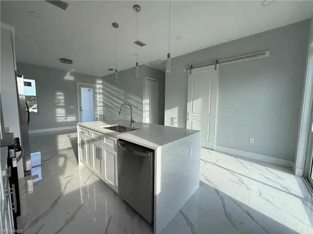Kitchen with white cabinetry, light stone countertops, a center island with sink, stainless steel appliances, and a barn door