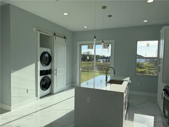Kitchen with light stone countertops, a center island with sink, a barn door, stove, and light marble finish flooring