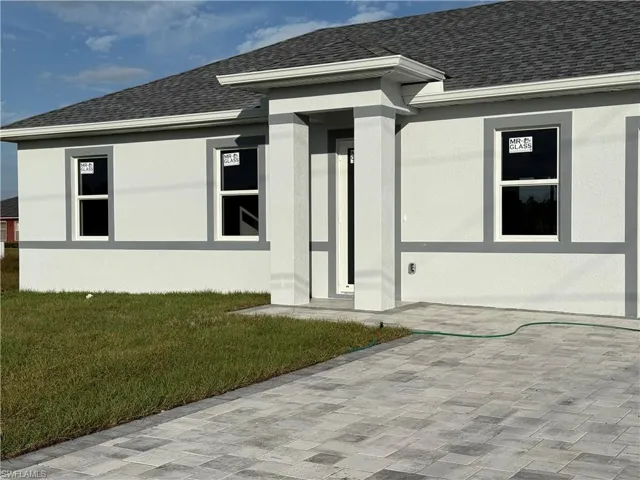 Entrance to property with roof with shingles, a yard, and stucco siding