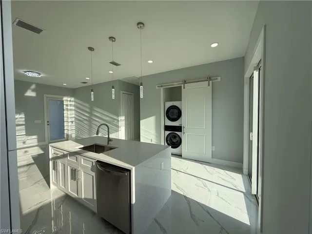 Kitchen with a barn door, white cabinetry, stainless steel dishwasher, light stone counters, and decorative light fixtures