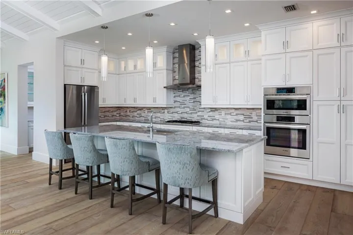 Kitchen with wall chimney exhaust hood, hardwood / wood-style flooring, pendant lighting, and appliances with stainless steel finishes