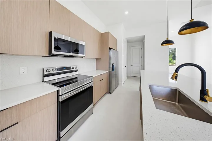Kitchen featuring modern cabinets, stainless steel appliances, light stone counters, hanging light fixtures, and light wood finish cabinetry