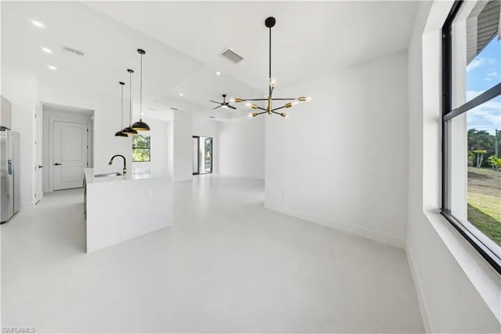 Kitchen with an island with sink, a chandelier, stainless steel refrigerator with ice dispenser, light stone counters, and open floor plan