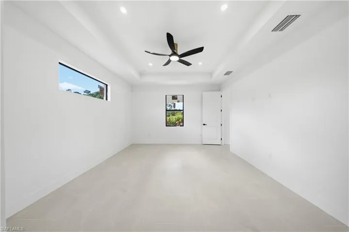 Empty room featuring healthy amount of natural light, a tray ceiling, ceiling fan, and recessed lighting