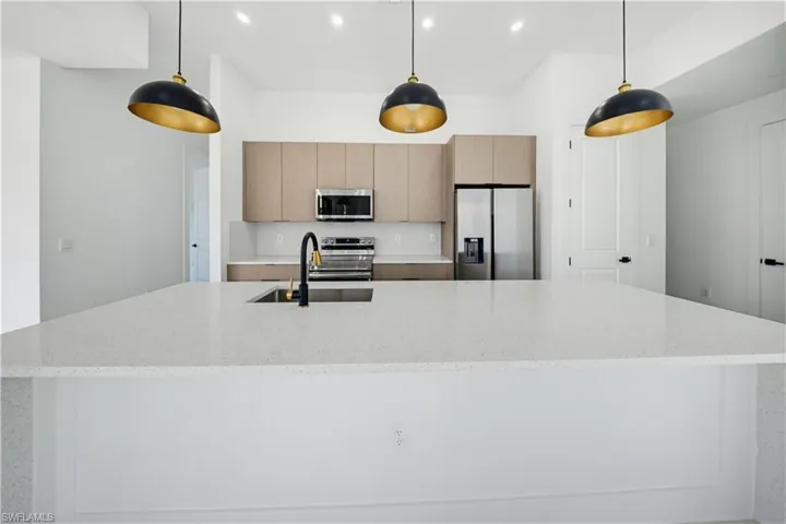 Kitchen featuring hanging light fixtures, light stone counters, stainless steel appliances, and a large island with sink