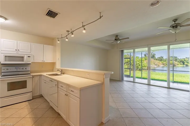 Kitchen with white appliances, light tile patterned floors, a peninsula, a water view, and white cabinetry