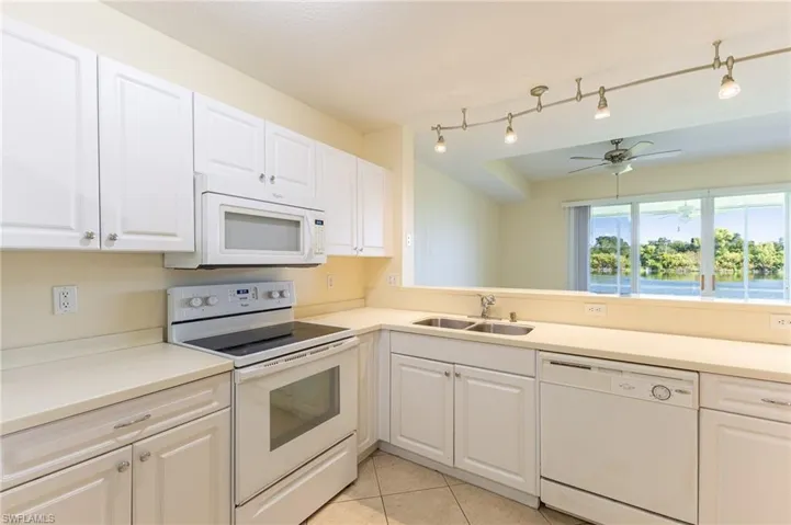 Kitchen with white appliances, white cabinets, light countertops, light tile patterned floors, and a ceiling fan