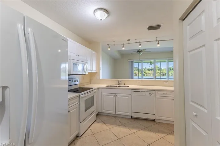 Kitchen featuring white appliances, white cabinets, light tile patterned floors, light countertops, and ceiling fan