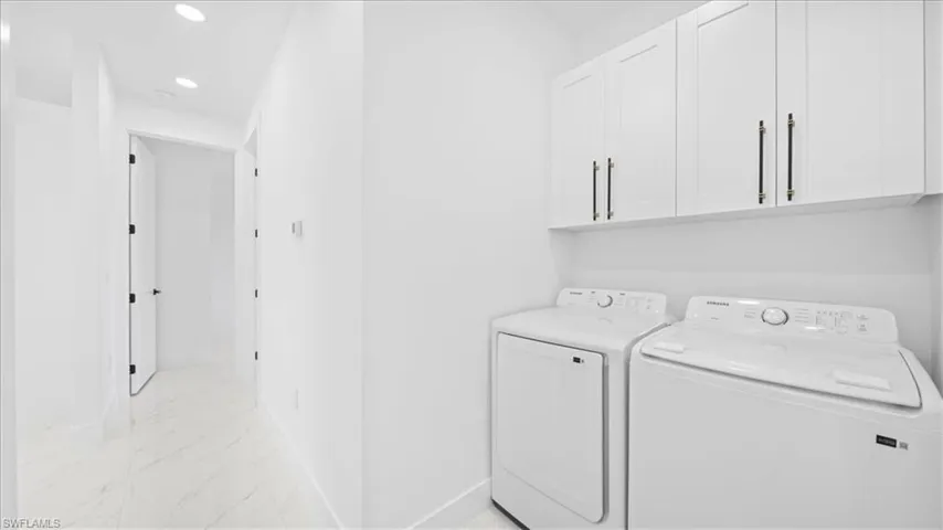 Laundry room featuring cabinet space, recessed lighting, washing machine and clothes dryer, and light marble finish flooring