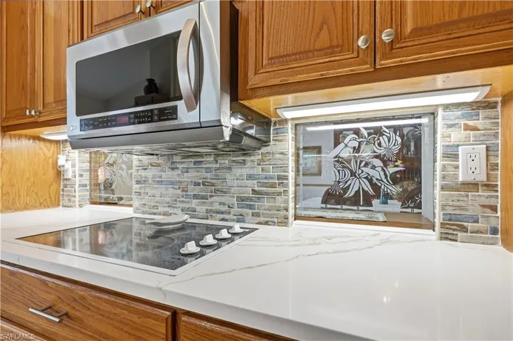 Kitchen featuring solid wood cabinetry, stainless steel microwave, electric cooktop, and tasteful backsplash, pass-thru to dining room