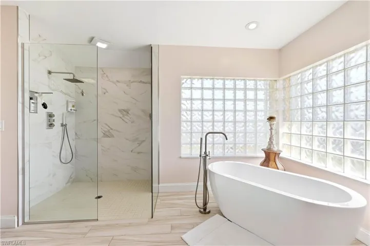 Full bathroom featuring a marble finish shower, a freestanding tub, Stainless steel fixtures, light tile floors and real glass blocks.