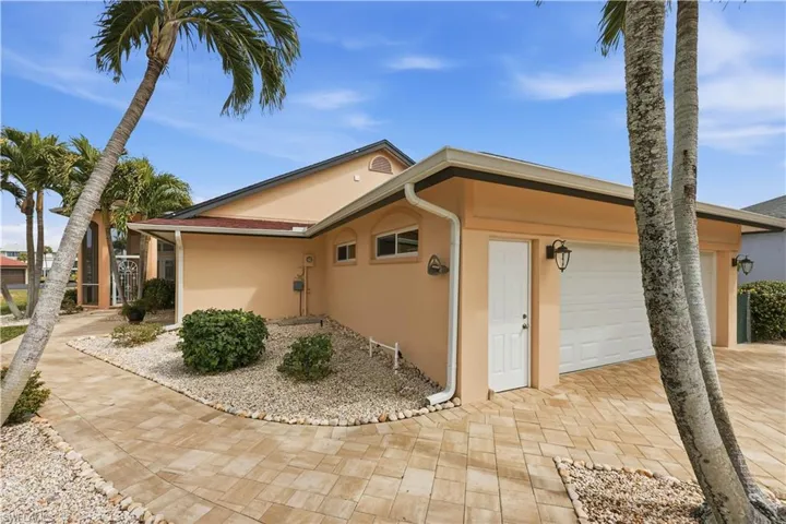 View of property exterior featuring stucco siding, paver driveway and walkway, garage and side door. Landscaping.