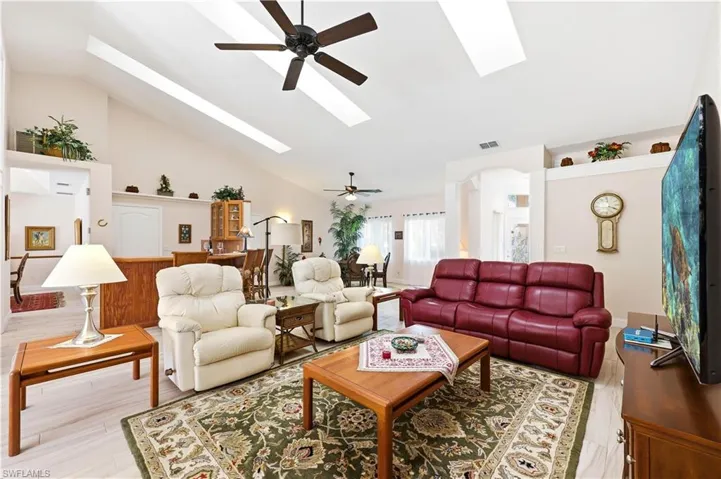 Living room featuring ceiling fans, skylights, tile floors, and vaulted ceiling.