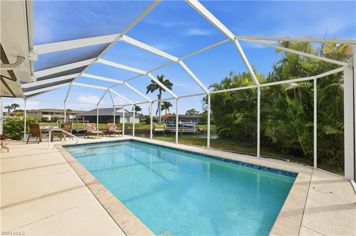 Saltwater heated Swimming pool featuring screen enclosure, large sunning area, and a view of the canal.