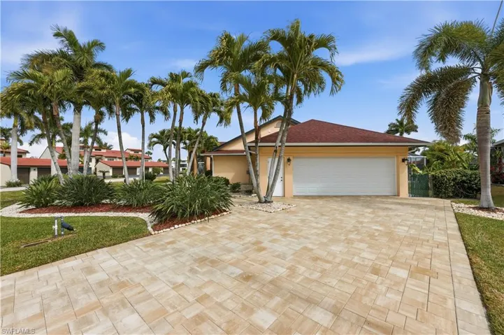 View of an Oversized Side Entrance Garage and one of two Side Doors, Paver Driveway, Stucco siding, and mature Landscaping with lots of palm trees and Bird of Paradise.