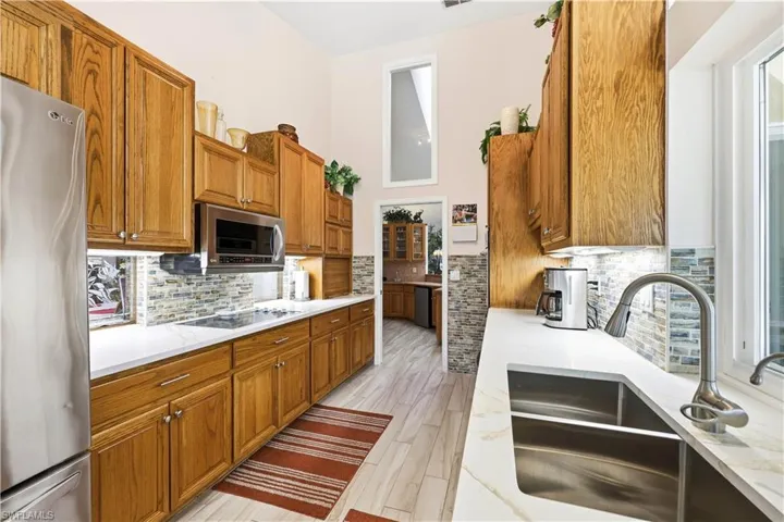 Kitchen with solid wood cabinetry, stainless steel appliances, quartz counters, light tile floors, and a high ceiling
