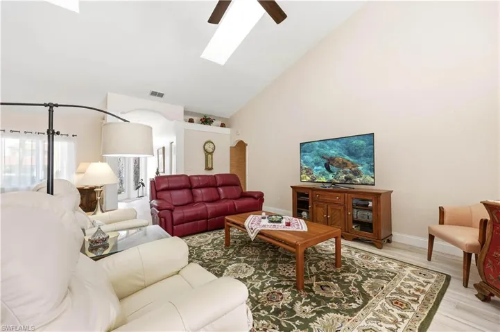 Living room with tile floors, skylights, a ceiling fan, and lofted ceiling.
