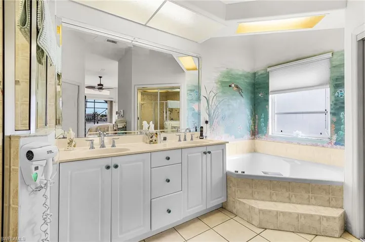 Full bath with double vanity, ensuite bath, a garden tub, ceiling fan, and light tile patterned flooring