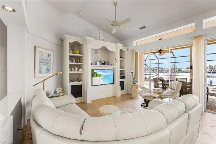 Living room featuring a ceiling fan, lofted ceiling, light tile patterned floors, and built in shelves