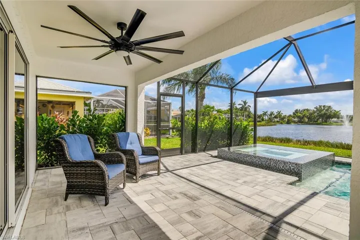 View of patio with a water view, ceiling fan, glass enclosure, and an in ground hot tub