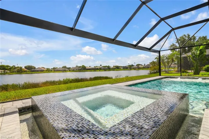 View of swimming pool featuring glass enclosure, an in ground hot tub, and a water view
