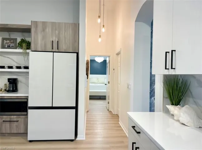 Kitchen with white fridge, light hardwood / wood-style flooring, hanging light fixtures, white cabinetry, and stainless steel microwave