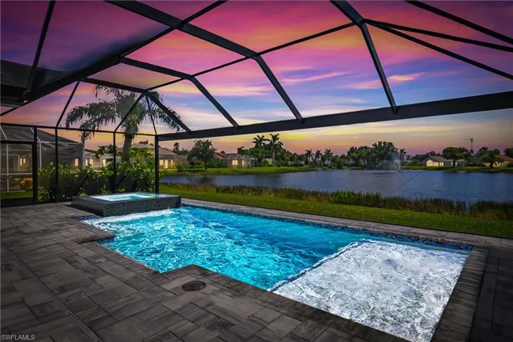 Pool at dusk with a lanai, an in ground hot tub, a patio, and a water view