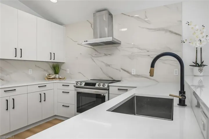 Kitchen featuring light hardwood / wood-style flooring, backsplash, wall chimney range hood, white cabinets, and stainless steel range with electric cooktop