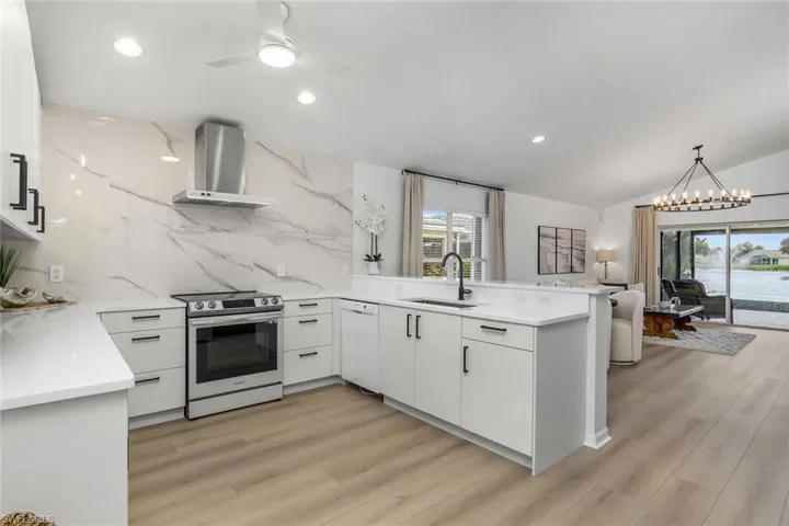 Kitchen with plenty of natural light, sink, electric stove, and wall chimney range hood