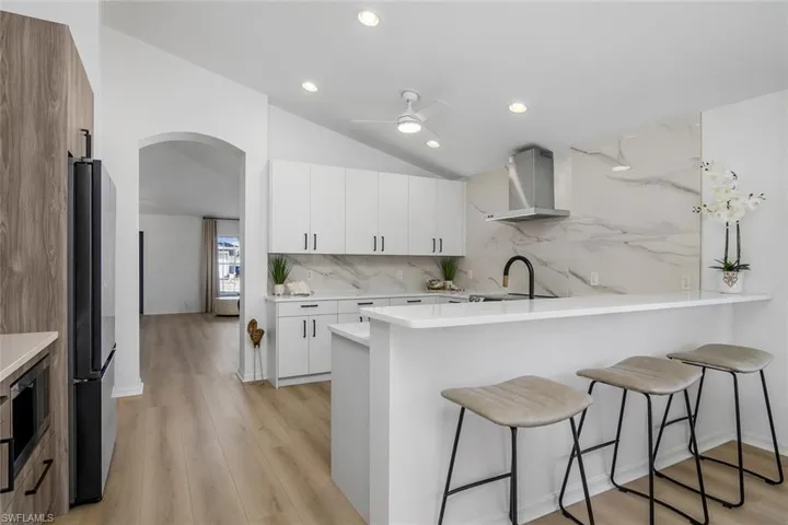 Kitchen featuring white cabinetry, light hardwood / wood-style flooring, stainless steel appliances, wall chimney exhaust hood, and lofted ceiling