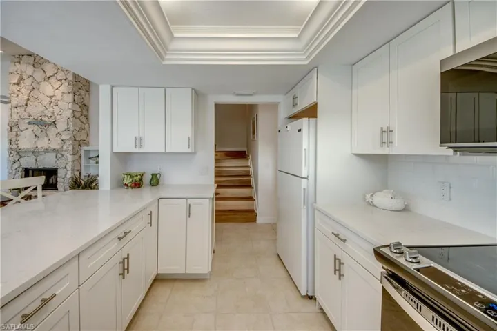 Kitchen featuring white cabinetry, a raised ceiling, stainless steel appliances, light stone counters, and a stone fireplace