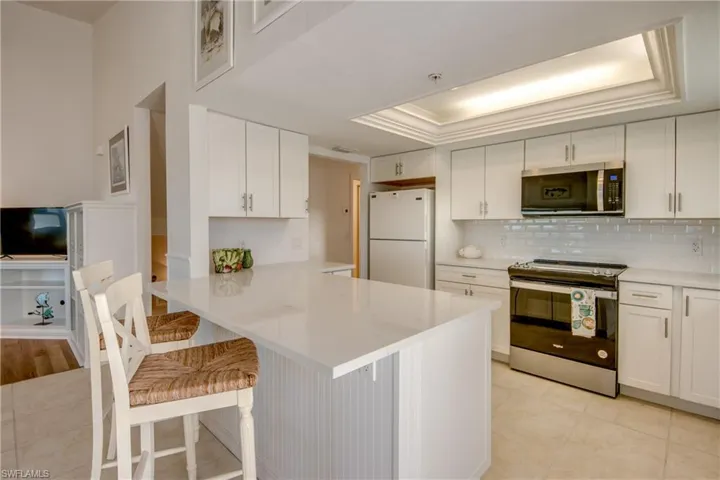 Kitchen with stainless steel appliances, white cabinets, a kitchen breakfast bar, a tray ceiling, and a peninsula