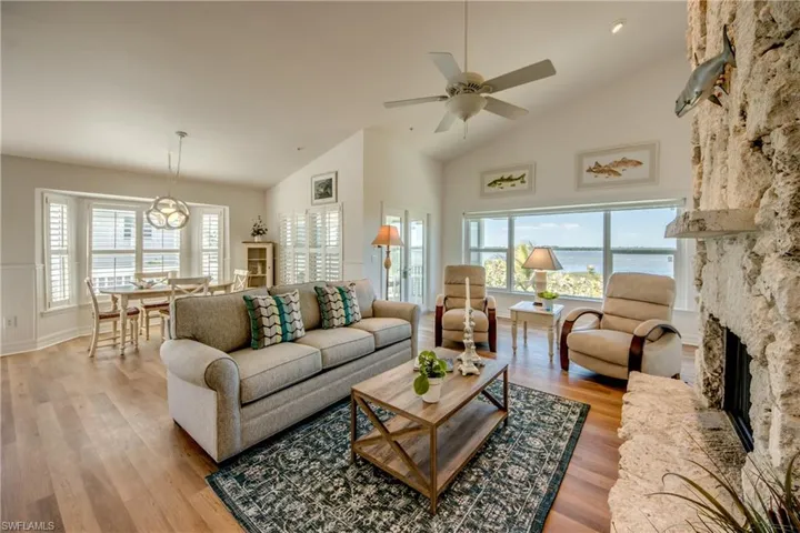 Living area featuring vaulted ceiling, a fireplace, a ceiling fan, wood finished floors, and a water view