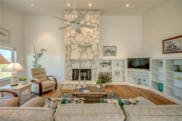 Living room with a high ceiling, wood finished floors, a stone fireplace, recessed lighting, and ceiling fan