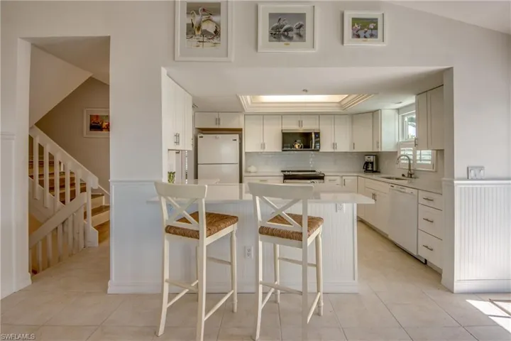 Kitchen with white cabinets, white appliances, a breakfast bar, decorative backsplash, and a peninsula