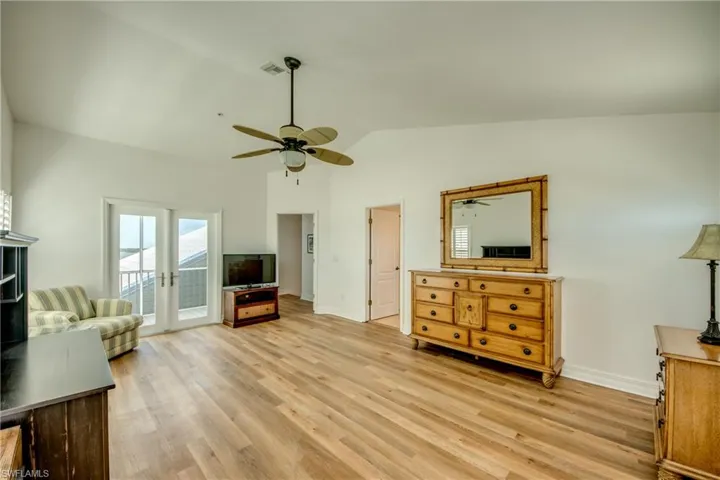 Primary suite with french doors, light wood-type flooring, vaulted ceiling, and a ceiling fan
