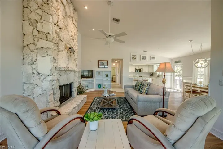 Living room featuring wood finished floors, a stone fireplace, suspended lighting, ceiling fan, and lofted ceiling