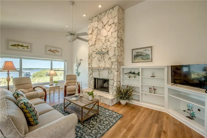 Living room with a stone fireplace, light wood-type flooring, a ceiling fan, lofted ceiling, and a water view