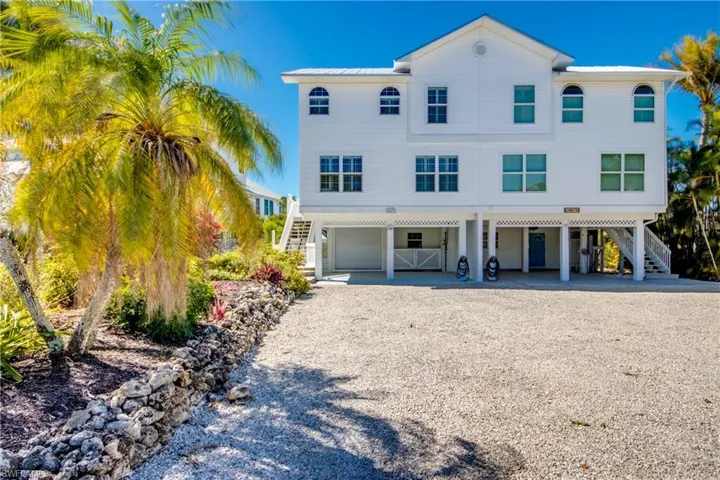 Raised beach house with a carport, driveway, a patio, a garage, and a metal roof