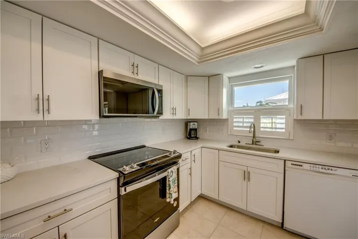 Kitchen with stainless steel appliances, white cabinetry, light stone counters, ornamental molding, and light tile patterned floors