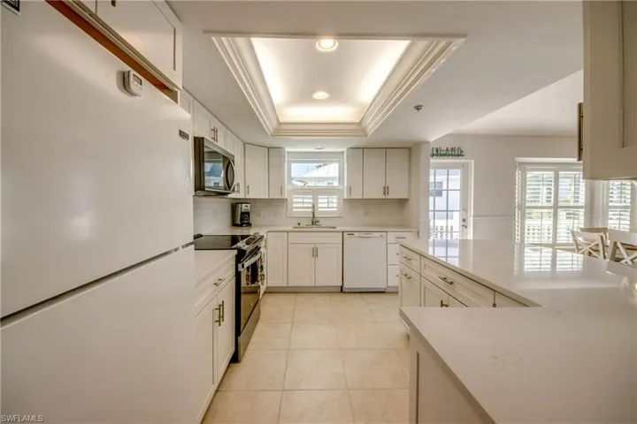 Kitchen featuring white appliances, white cabinets, a raised ceiling, light stone countertops, and light tile patterned floors