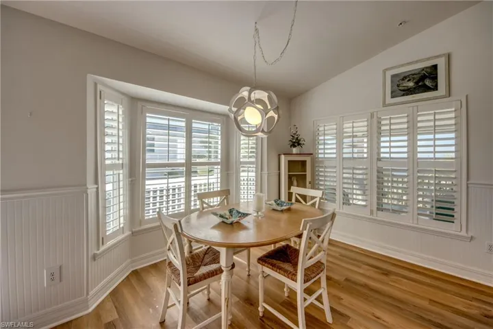 Dining space with wainscoting, lofted ceiling, light wood-style flooring, and hanging lights