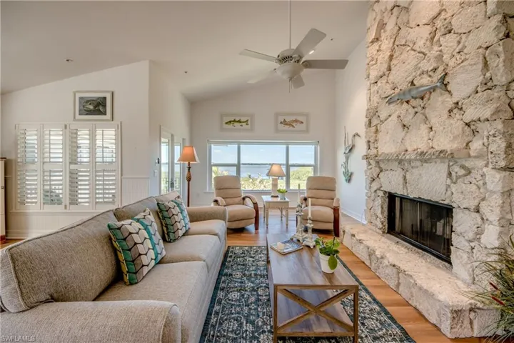 Living room featuring a stone fireplace, wood finished floors, ceiling fan, and lofted ceiling