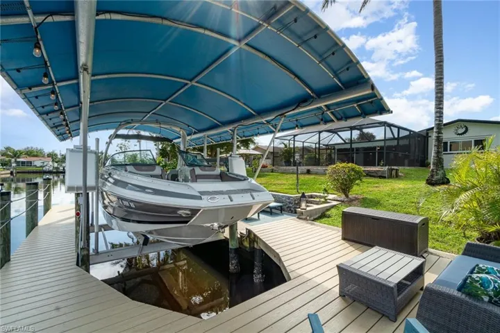 View of dock featuring a water view, glass enclosure, and a lawn