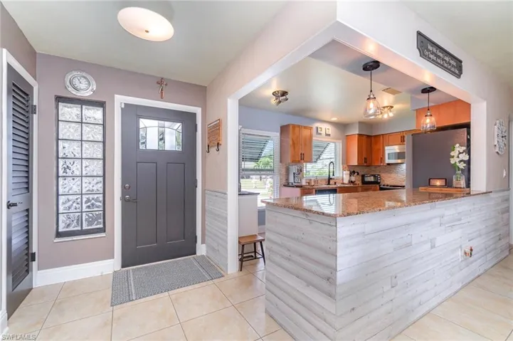 Kitchen featuring appliances with stainless steel finishes, light stone counters, light tile patterned flooring, decorative light fixtures, and kitchen peninsula