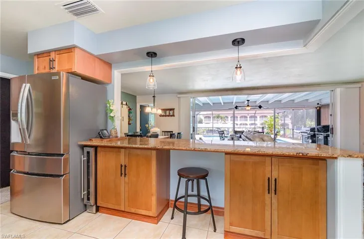 Kitchen featuring light tile patterned flooring, decorative light fixtures, stainless steel fridge, kitchen peninsula, and light stone countertops